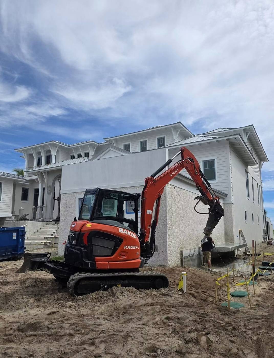 Baker Demolition & Construction mini excavator performing concrete demolition beside a coastal home