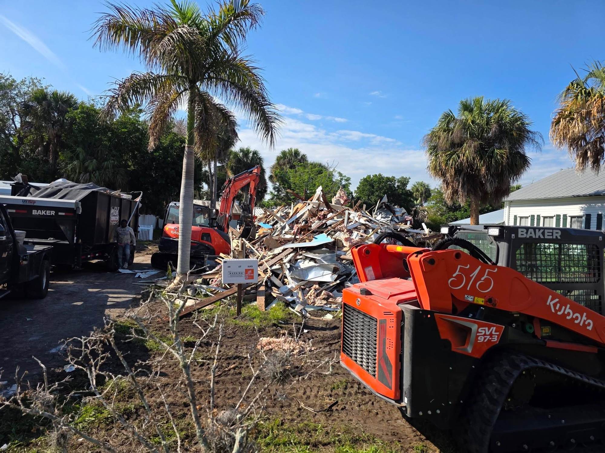 Demolition debris pile with Baker Demolition & Construction dump trailer, excavator and skid steer on site
